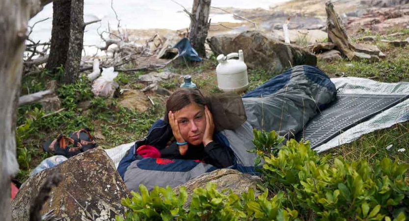 a student rests on a sleeping pad near the shore on an outward bound expedition in maine